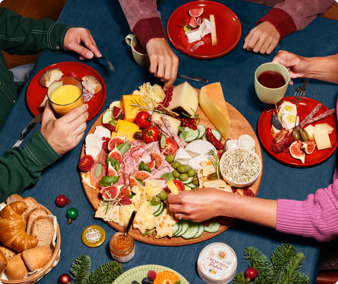 Mehrere Hände bedienen sich an einem festlichen Charcuterie-Board zum Adventsbrunch.